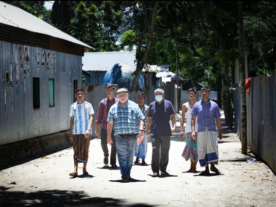 A group of people walking toward the camera on a dusty street in Bangladesh