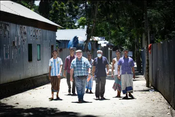 A group of people walking toward the camera on a dusty street in Bangladesh